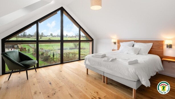 Ein Schlafzimmer mit einem großen Oberlicht, einem Bett, einem Sessel und Blick auf eine grüne Landschaft.