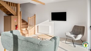 Ein modernes Wohnzimmer mit Treppe, einem Wand-Fernseher und zwei Sesseln.