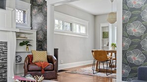 Un salon avec une cheminée, un coin repas avec une table et des chaises, et une grande fenêtre avec des encadrements blancs.