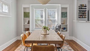 Un espace repas comprenant une table en bois, des chaises, un luminaire suspendu et des étagères intégrées ornées d’objets décoratifs.