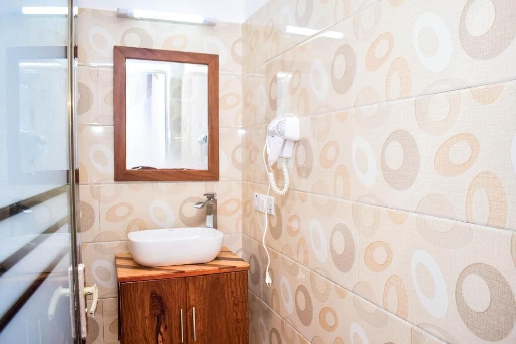 A bathroom with a wooden vanity, a white sink, and a mirror above it. There is a hairdryer on the wall.