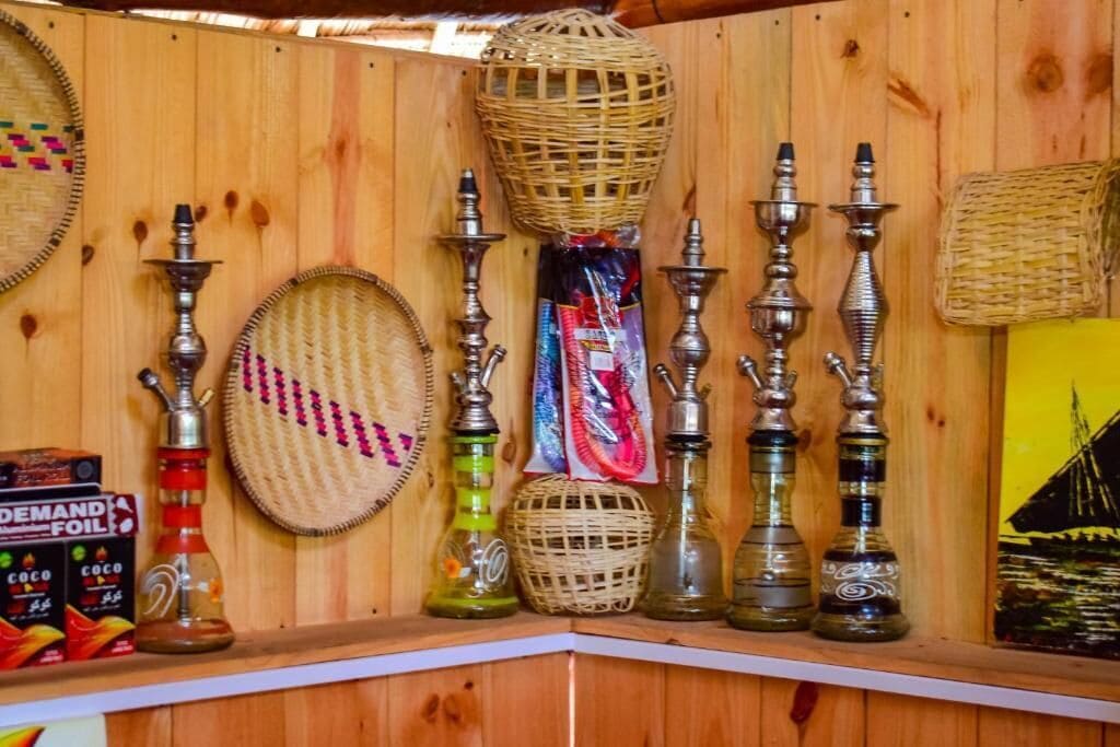 A wooden wall with various items including woven baskets, metal hookahs, and a bottle of Coco Demitasse.