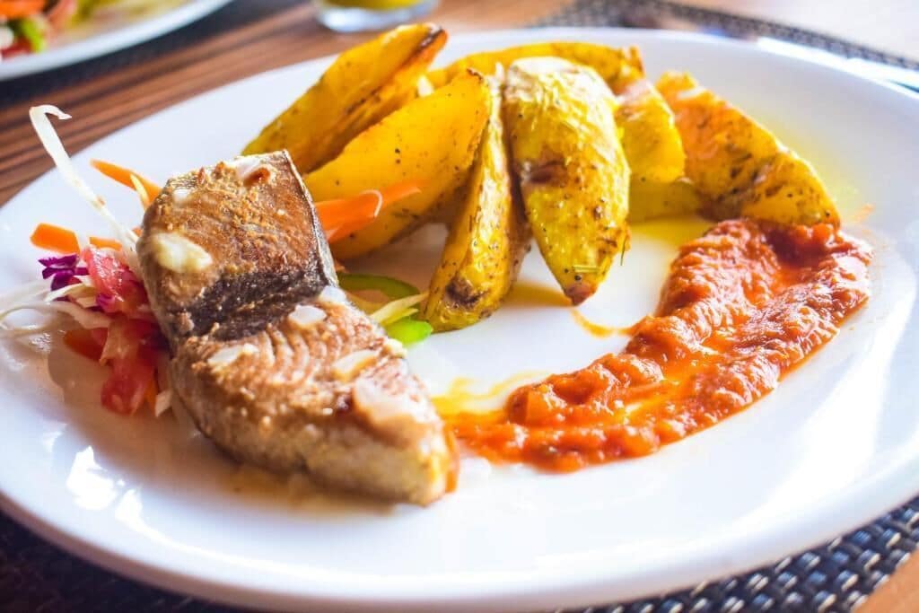 A plate with a piece of fish, roasted potatoes, and a tomato-based sauce.