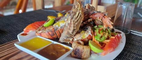 A seafood platter with various grilled items and dipping sauces on a white plate.