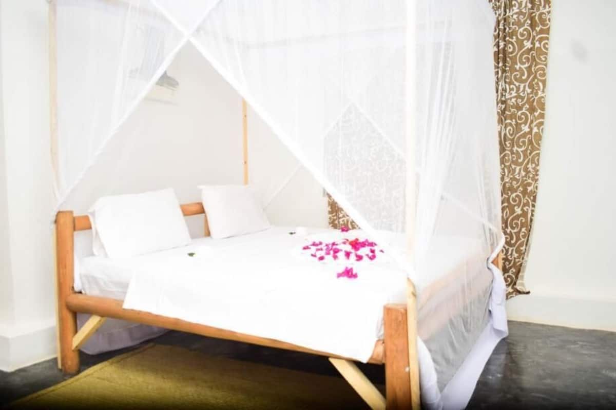 A bed with a white bedspread and a canopy, a wooden headboard, and a patterned curtain.