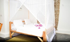 Ein Bett mit weißer Bettdecke und Baldachin, ein hölzernes Kopfende und ein gemustertes Vorhang.