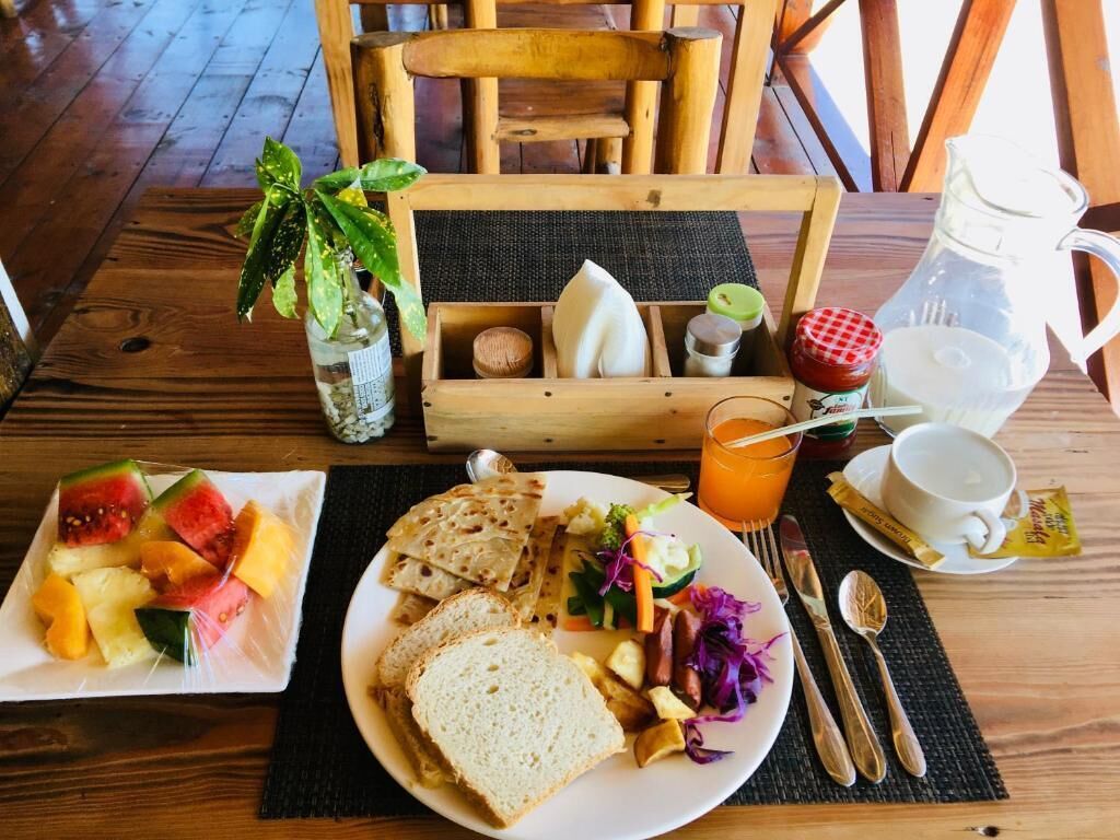 A wooden dining table with a meal setup including a plate of bread, a fruit salad, a vegetable salad, and a pitcher of orange juice.