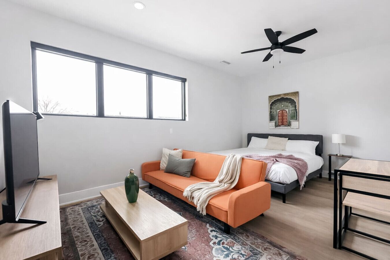 Ein modernes Schlafzimmer mit Bett, Sofa, Fernseher und Deckenventilator.