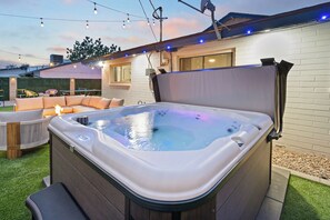 Ein Whirlpool mit Abdeckung, umgeben von einer Terrassenfläche mit einer Sitzecke und einem Tisch.