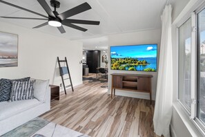Ein modernes Wohnzimmer mit Fernseher, Holzboden, Deckenventilator und Blick auf eine schöne Landschaft durch ein Fenster.