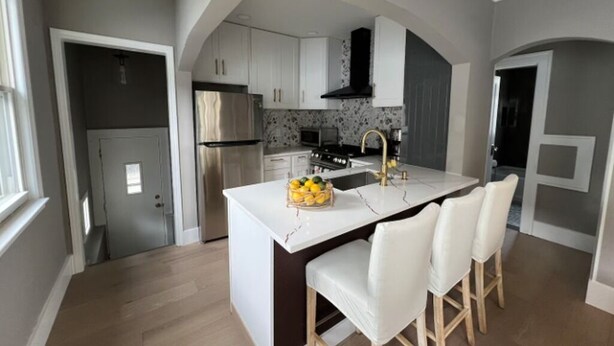 A modern kitchen with white cabinetry, a central island with bar stools, and a stainless steel refrigerator.