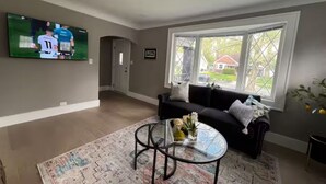 A living room with a black sofa, a glass coffee table, and a TV mounted on the wall.