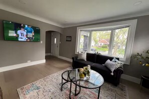 A living room with a black sofa, a glass coffee table, and a TV mounted on the wall. - Cute Modern Home with basement (Ferndale)