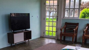A dining area with a white table set for four, surrounded by chairs, a television on a cabinet, and a door leading outside. - Comfortable beachfront retreat, 1 minute walk. Secure condominium - Orla 500 (Cabo Frio)
