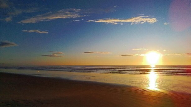 A beach with the sun setting over the horizon, reflecting on the water. - Comfortable beachfront retreat, 1 minute walk. Secure condominium - Orla 500 (Cabo Frio)
