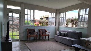 A spacious room with a grey sofa, two wooden chairs, a TV on a stand, and a table. - Comfortable beachfront retreat, 1 minute walk. Secure condominium - Orla 500 (Cabo Frio)