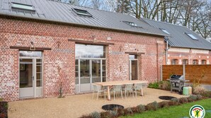 Un bâtiment en briques doté de grandes fenêtres et d’un patio aménagé avec une table et des chaises.