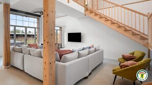 Un salon spacieux avec un grand canapé, un téléviseur fixé au mur et un escalier en bois.