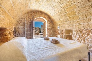 Un dormitorio de paredes de piedra con una cama grande, un arco de entrada y vistas al exterior.