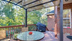 Une terrasse couverte avec une table ronde, un barbecue et un bâtiment en briques en arrière-plan.