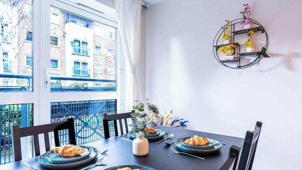 A dining table with plates of croissants, a vase with flowers, and a wall-mounted shelf with potted plants. - Spacious 2BR Flat - Bounds Green, Private Parking (London)