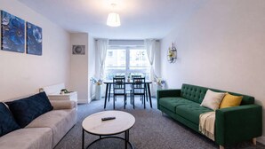 A living room with a green sofa, a beige sofa, a round coffee table, and a dining area with a table and chairs. - Spacious 2BR Flat - Bounds Green, Private Parking (London)