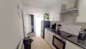 Een kleine keuken met witte kastjes, een zwart aanrecht, een inbouwoven en een kleine prullenbak.