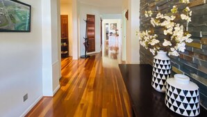 A hallway with wooden flooring, a dark wall with a geometric pattern, and two vases with a black and white design. - Cascade Cottage: Spacious Family Retreat in Keysborough Garden Parking Sleeps 8 (Keysborough)