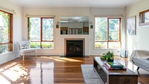A spacious living room with a fireplace, large windows, and a cozy seating area. - Cascade Cottage: Spacious Family Retreat in Keysborough Garden Parking Sleeps 8 (Keysborough)