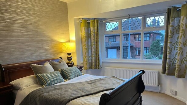 A bedroom with a bed, a nightstand, a lamp, a window with curtains, and a radiator. - Uphill Lincoln Home, Near Cathedral and Castle (Lincoln)