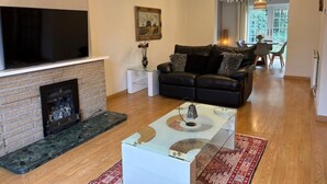 A living room with a fireplace, a black leather sofa, a glass coffee table, and a flat-screen TV mounted above the fireplace. - Uphill Lincoln Home, Near Cathedral and Castle (Lincoln)