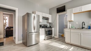 A modern kitchen with stainless steel appliances, white cabinetry, and a flat-screen TV. - Walk to Trolley District: Olde Towne East Retreat (Columbus)