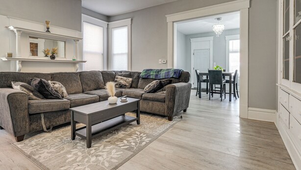 A living room with a sectional sofa, a coffee table, and a fireplace. There is a dining area in the background with a chandelier. - Walk to Trolley District: Olde Towne East Retreat (Columbus)