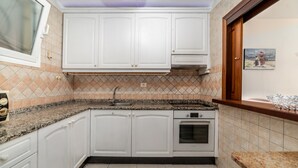 Cozinha com armários brancos, bancada de granito, forno embutido e janela com vista para o exterior.