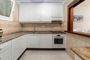 A kitchen with white cabinets, a granite countertop, a built-in oven, and a window with a view of the outdoors. - Tropical Holiday Apartment (Los Cristianos)