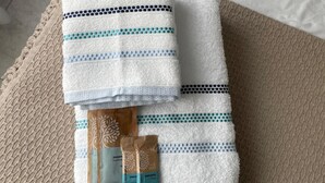 Ein ordentlich gefaltetes weißes Handtuch mit blauen Streifen und eine braune Seifentasche auf einer strukturierten beigefarbenen Matte.