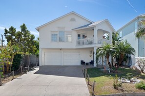 A two-story house with a front garage, a balcony on the second floor, and a well-maintained lawn with palm trees. - Someday Sunset by the Bay Lower Level (South Padre Island)