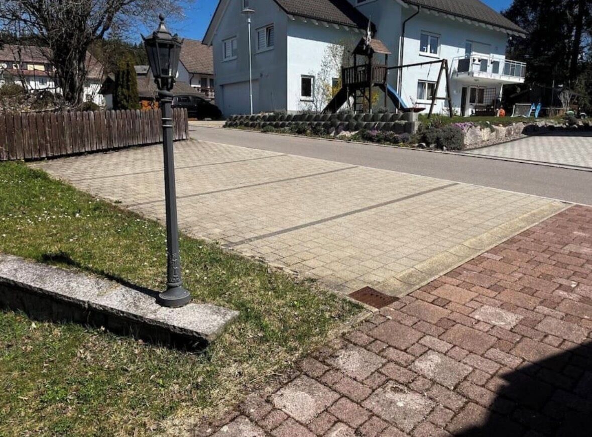 Un chemin pavé, un lampadaire en métal, une clôture en bois et une maison avec un balcon en arrière-plan.