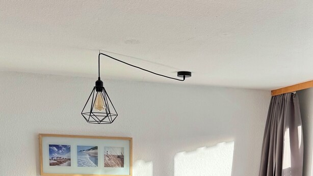 Ein ordentlich gemachtes Bett mit Kopfteil, ein Nachttisch mit einer Glasdose und ein Bilderrahmen an der Wand.