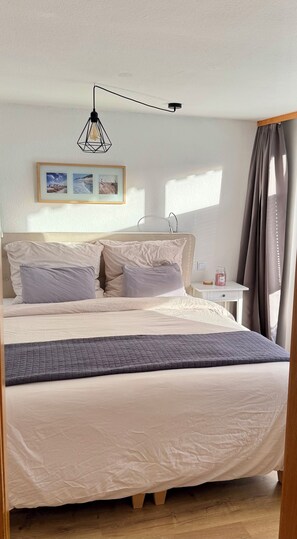 A neatly made bed with a headboard, a bedside table with a jar, and a picture frame on the wall.