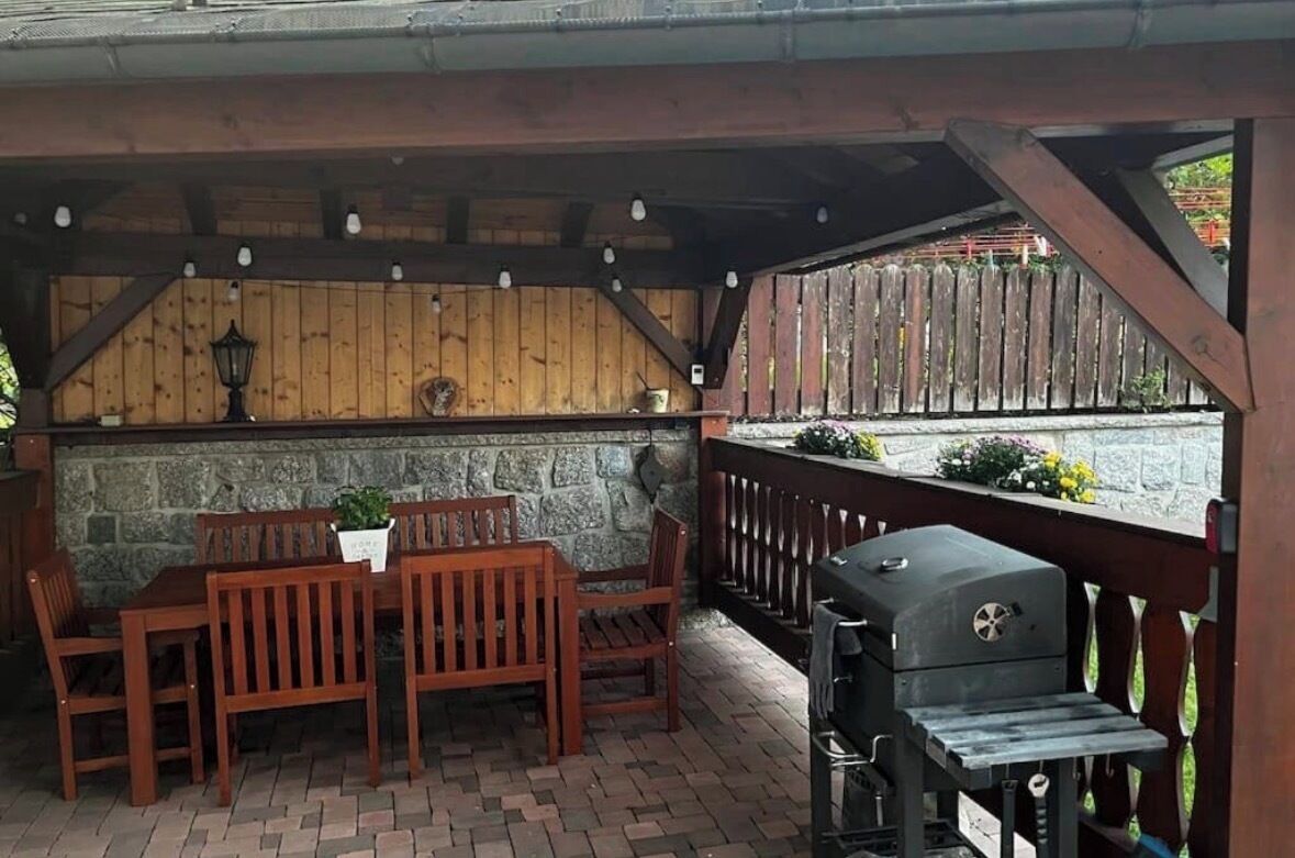 Un patio cubierto con pared de piedra, mobiliario de madera y una parrilla.