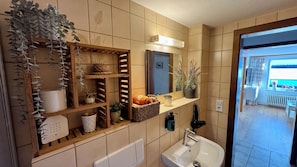 Un baño con estante de madera, espejo, lavabo y ventana.