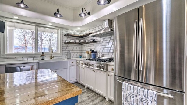 Una cocina moderna con armarios blancos, un refrigerador de acero inoxidable, una encimera de madera y una estufa a gas.