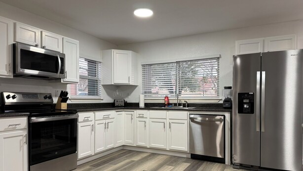 A modern kitchen with white cabinets, stainless steel appliances, and a herringbone wood floor.