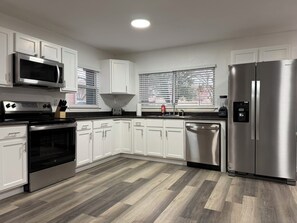 Una cocina moderna con armarios blancos, electrodomésticos de acero inoxidable y piso de madera en patrón de espiga.