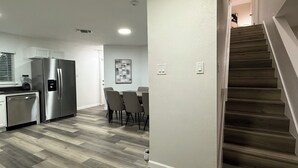 A modern kitchen with stainless steel appliances, a dining area with a table and chairs, and a staircase leading to another level.