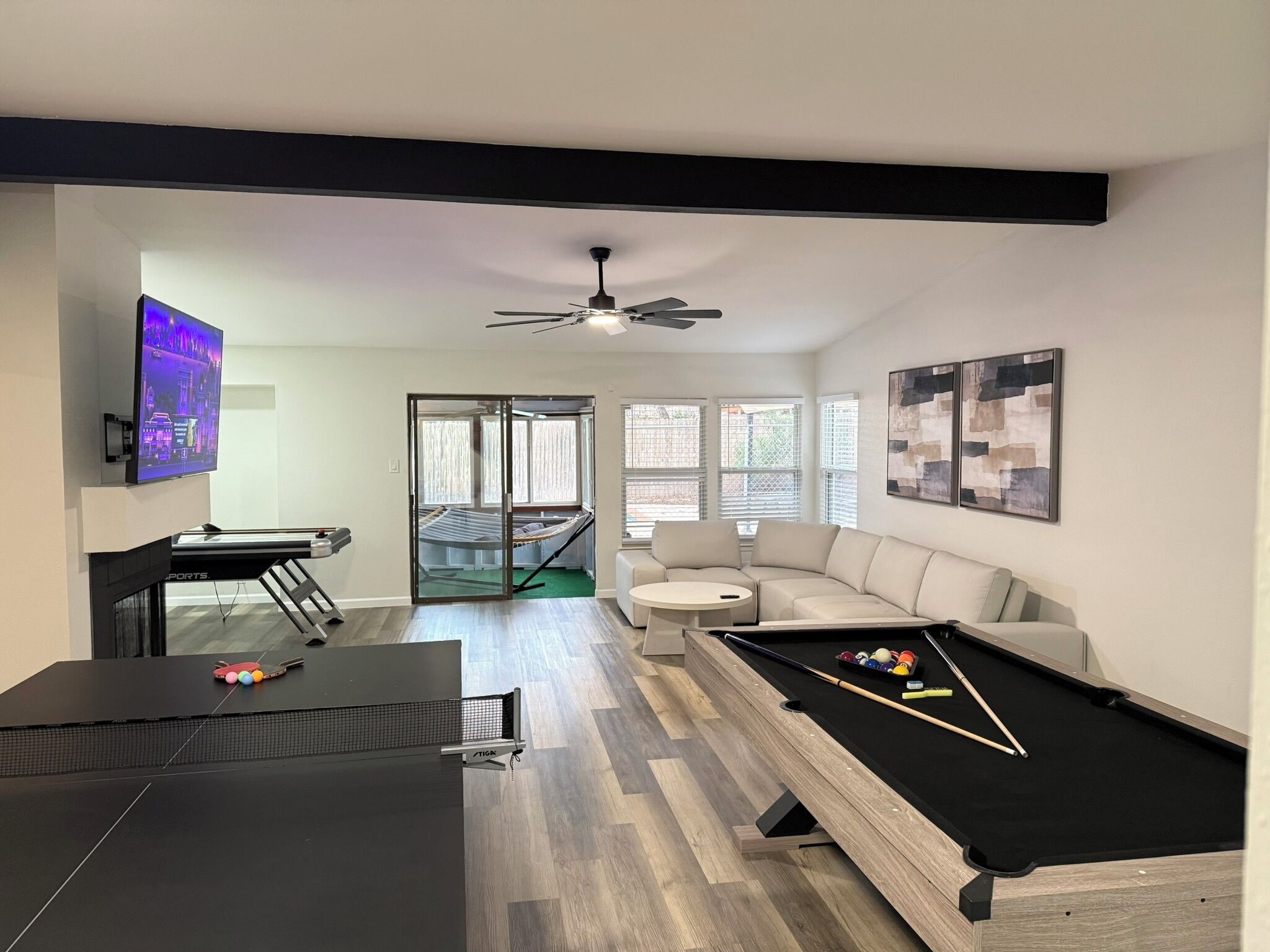Un salon moderne avec une table de billard, un canapé, un téléviseur et un ventilateur de plafond.