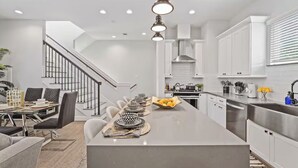 A modern kitchen with a central island, white cabinetry, and a staircase leading to an upper level.