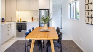 Una cocina moderna con armarios blancos, una isla central y un comedor con una mesa y sillas de madera.