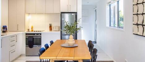 Una cocina moderna con armarios blancos, una isla central y un comedor con una mesa y sillas de madera.